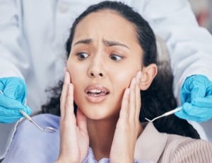 A woman looking anxious as a dentist approaches with dental tools, representing dental anxiety